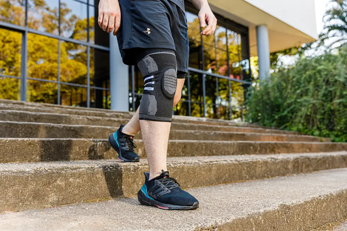 Pessoa descendo escada usando joelheira LegFix preta de compressão e tênis esportivos pretos