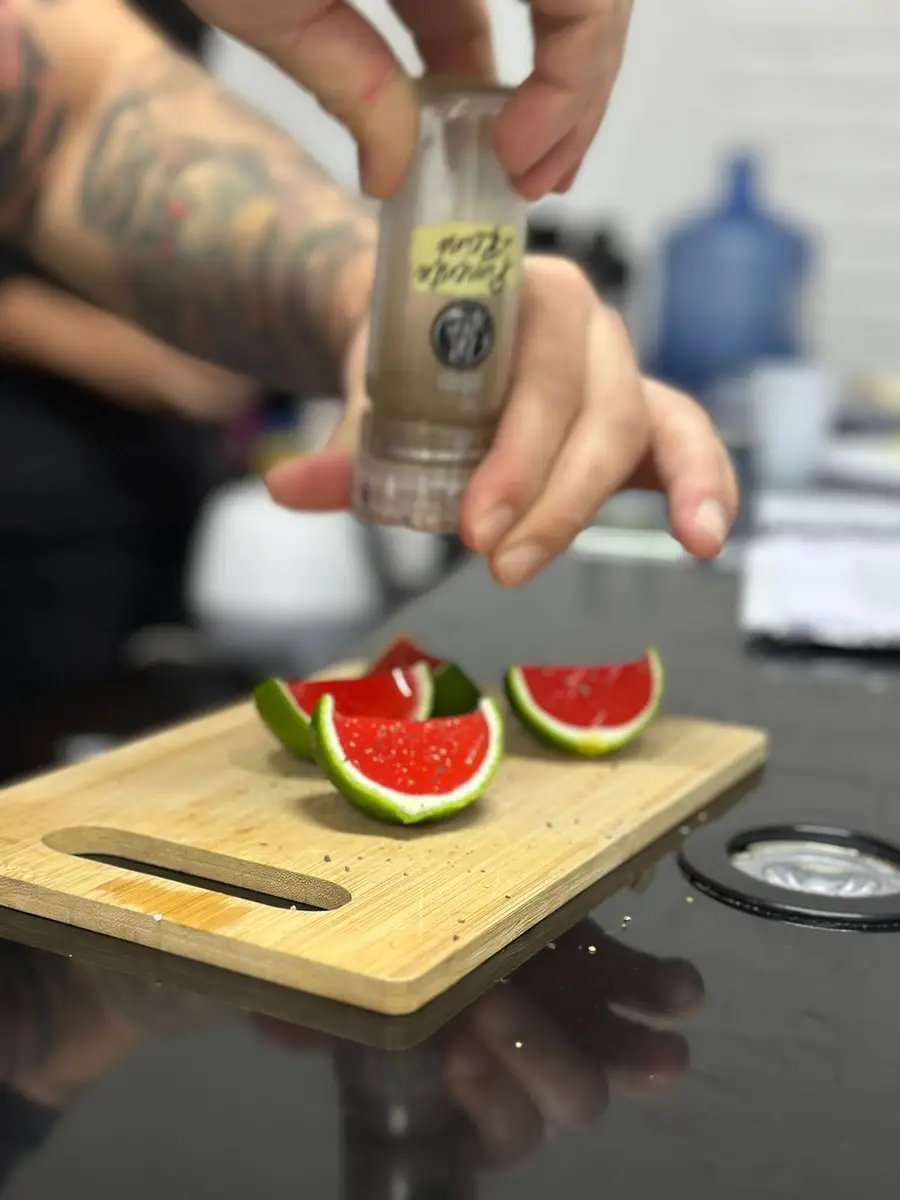 Mãos temperando gomos de limão com pimenta preta em moedor sobre tábua de madeira