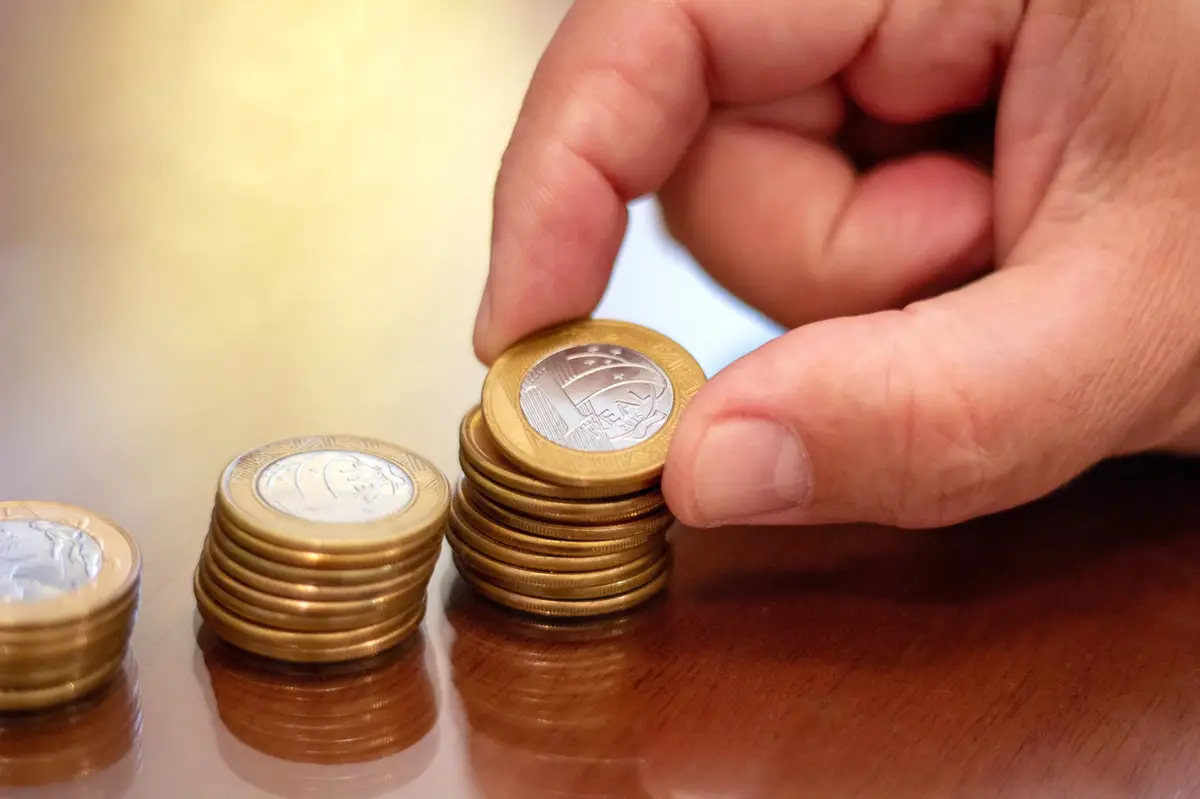 Mão empilhando moedas de real sobre superfície de madeira