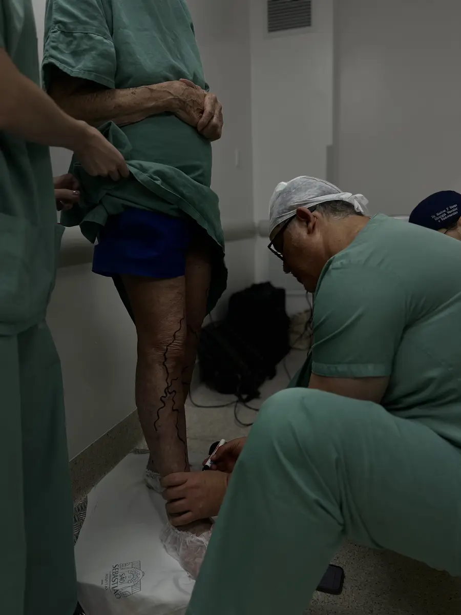 Dr. Marcelo Mandelli desenhando marcações em varizes na perna de paciente idoso