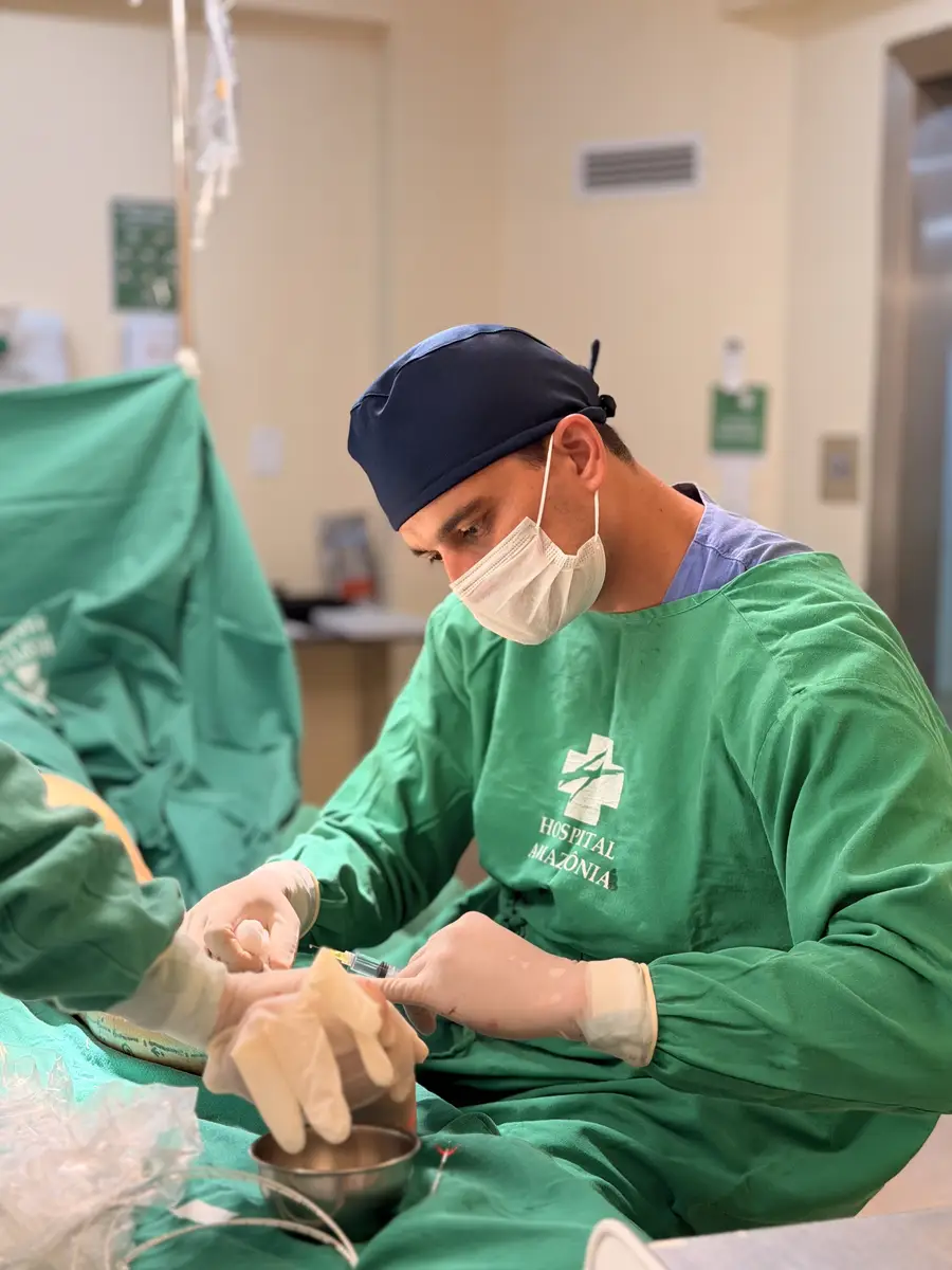 Médico cirurgião vascular realizando procedimento em ambiente hospitalar com roupas cirúrgicas verdes