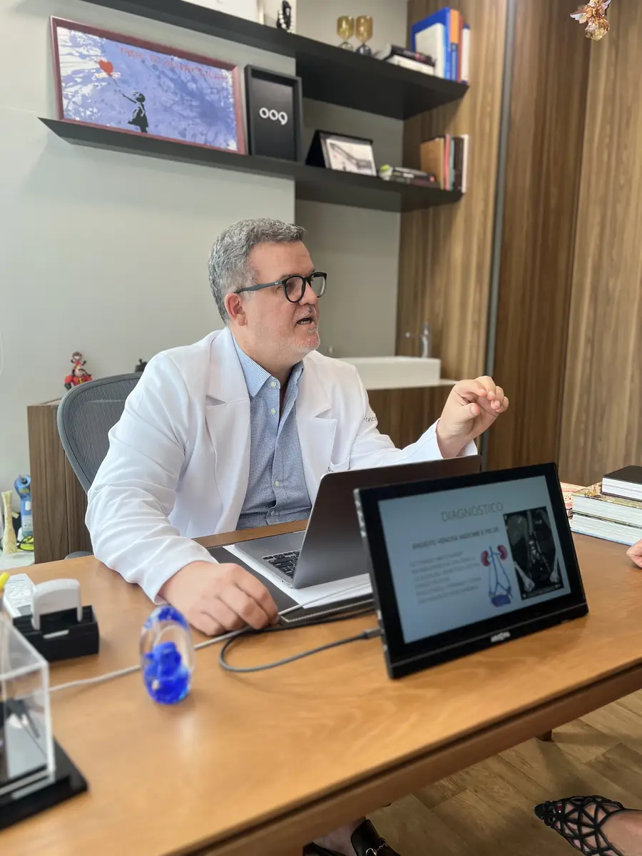 Dr. Marcelo Mandelli consultando paciente em escritório com tela mostrando diagnóstico vascular