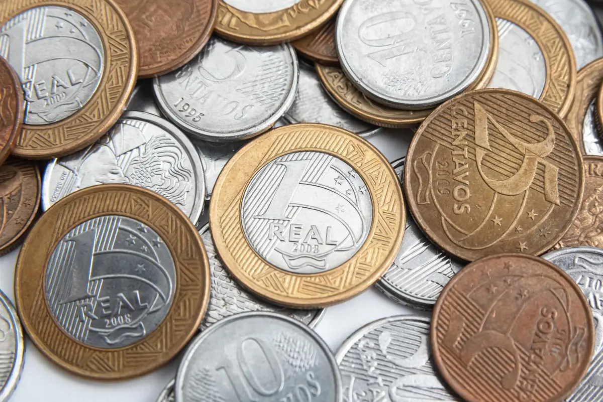 Moedas brasileiras de diferentes valores empilhadas e espalhadas
