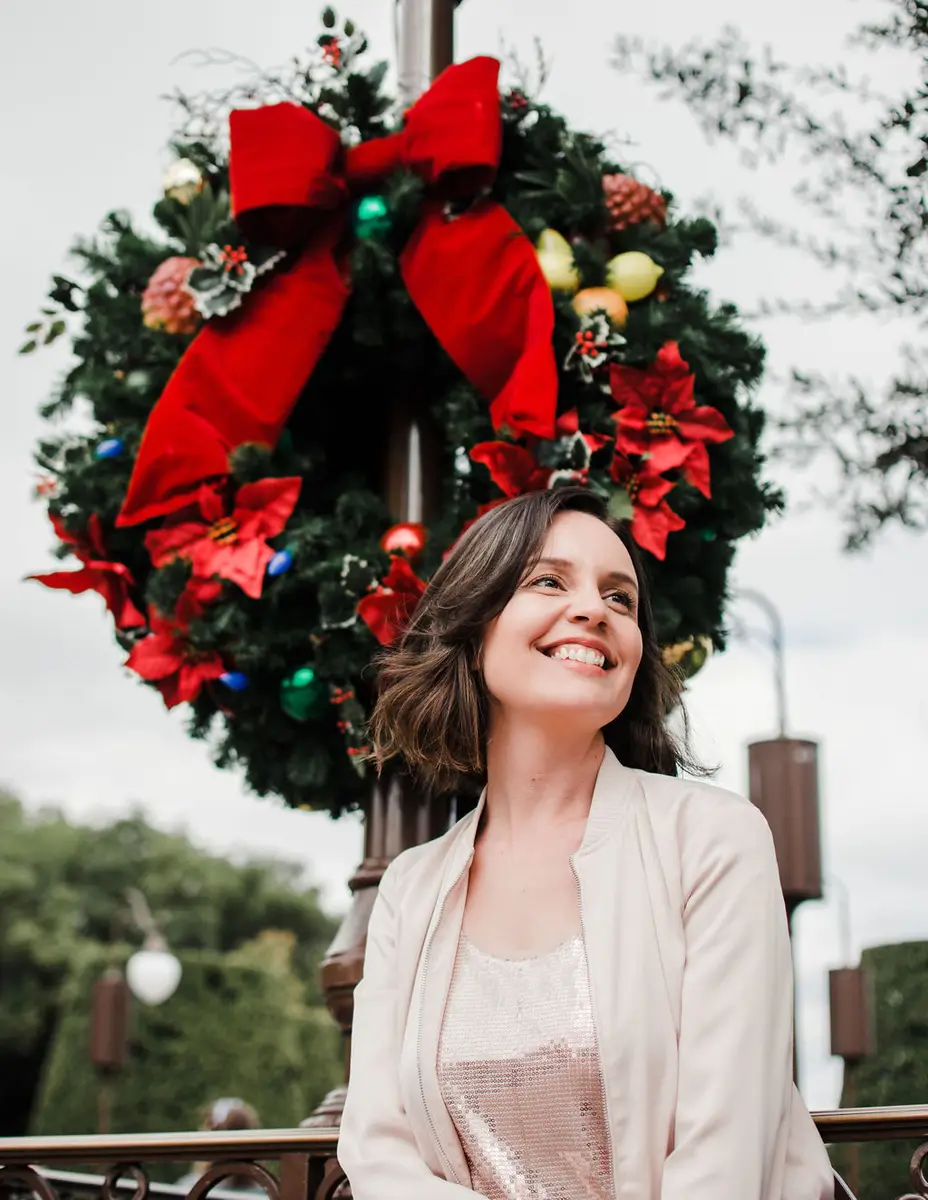 Mulher sorridente em frente a guirlanda natalina com laço vermelho grande