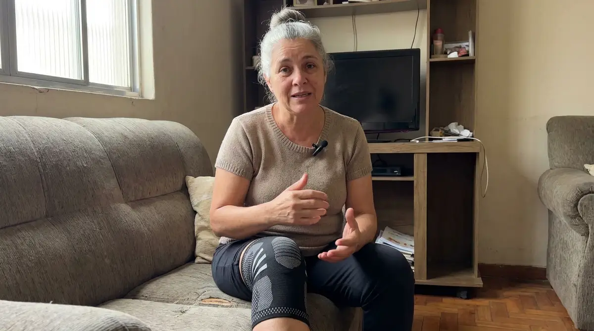 Mulher madura sentada no sofá usando joelheira de compressão LegFix no joelho direito