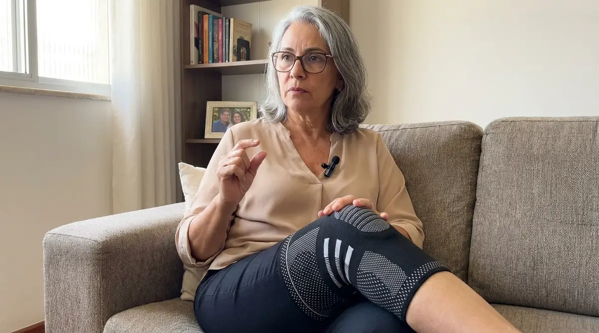 Mulher madura sentada no sofá usando joelheira de compressão LegFix preta e cinza