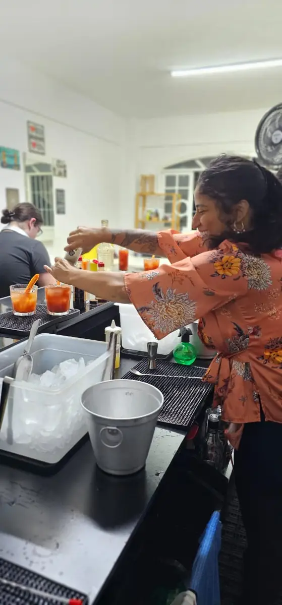Mulher preparando drinks em um bar com decoração branca e utensílios de bar