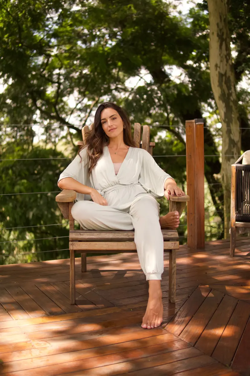 Mulher sentada relaxada em cadeira de madeira em um deck ao ar livre cercado por árvores