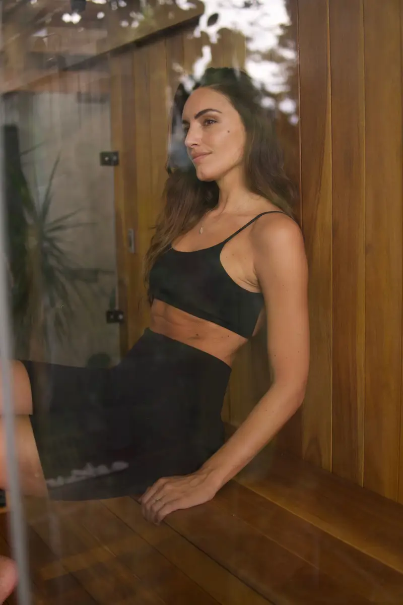 Mulher vestindo roupa preta, sentada relaxada em banco de madeira em spa