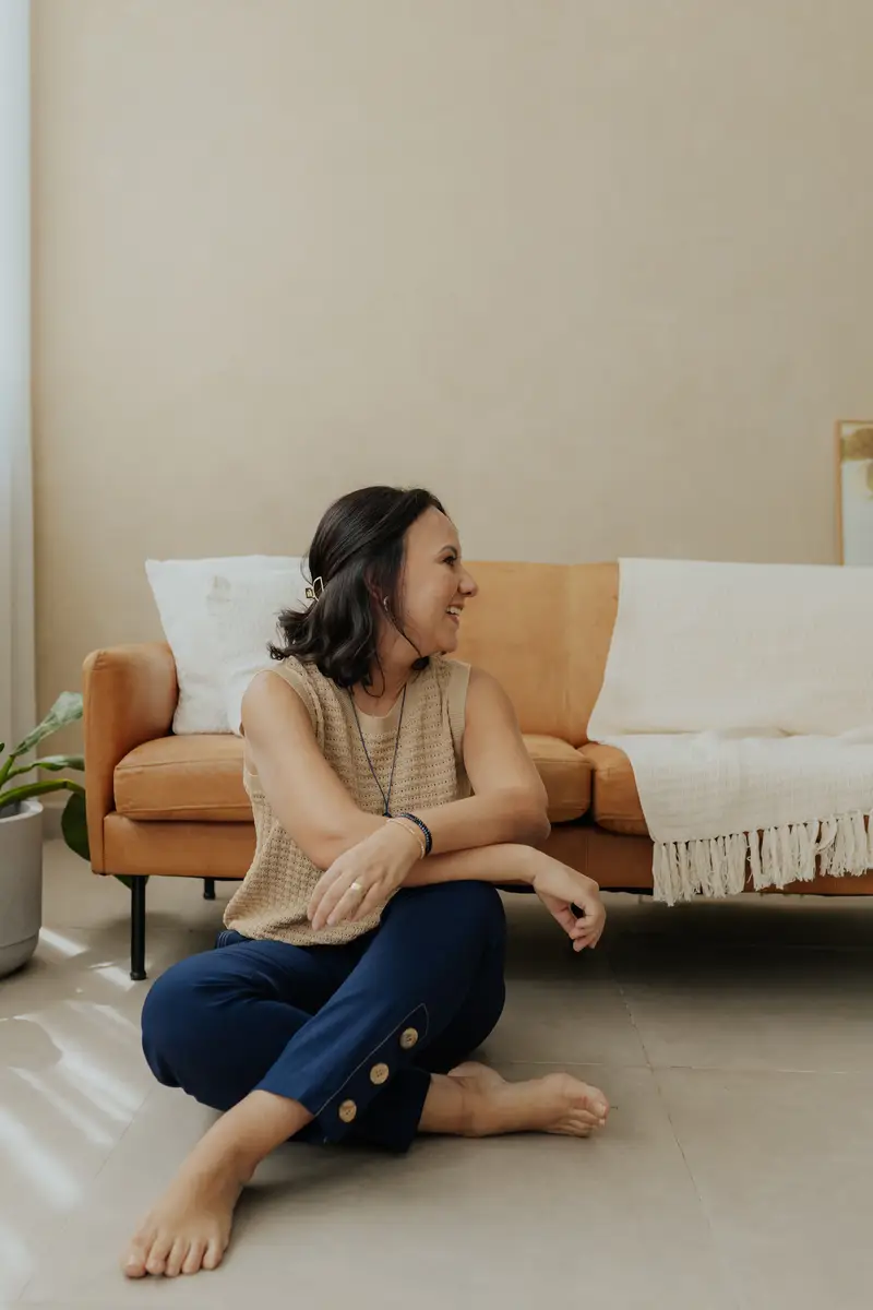 Mulher sentada no chão em uma sala com sofá marrom ao fundo