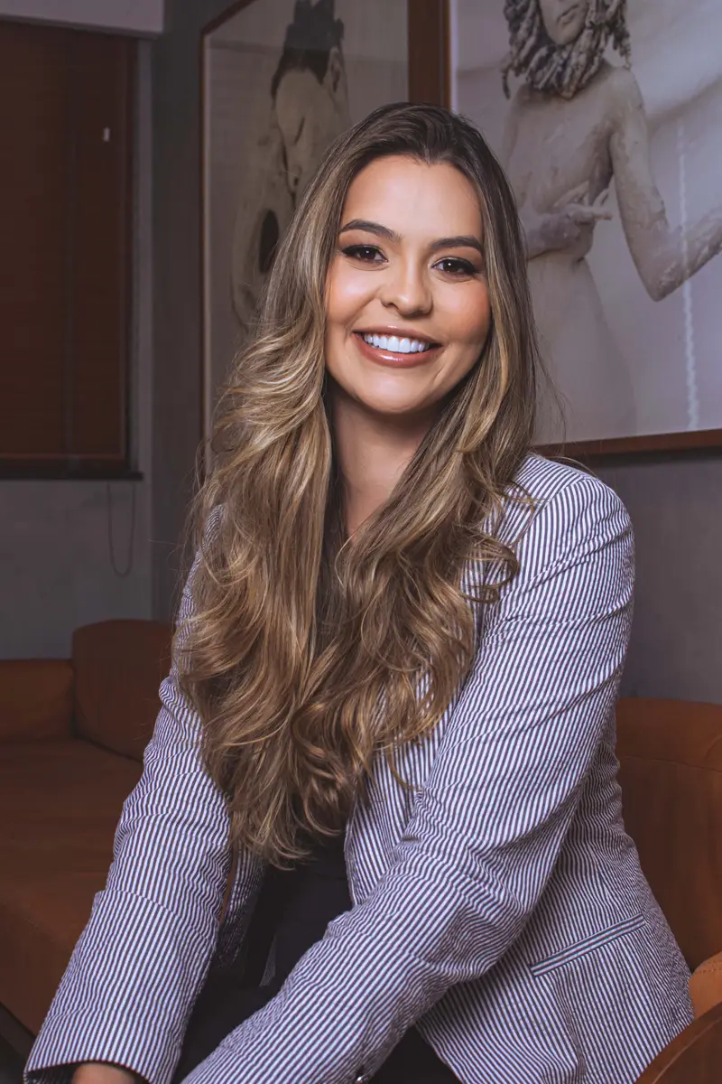 Mulher sorridente com cabelo longo e ondulado usando blazer listrado em ambiente interno elegante
