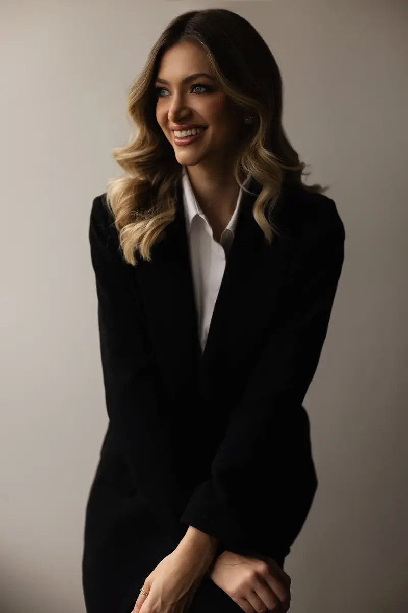 Mulher sorridente com blazer preto e camisa branca olhando para o lado