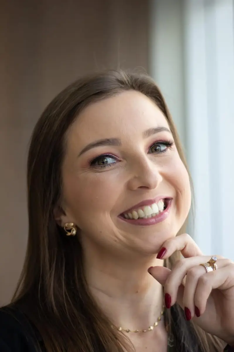 Mulher sorridente com unhas vermelhas e joias douradas perto do rosto