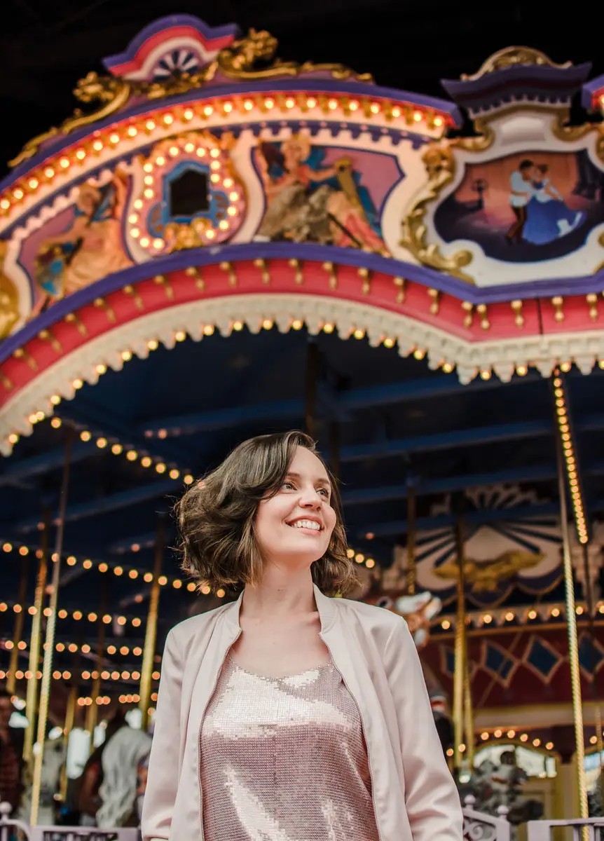 Mulher sorrindo em frente a um carrossel iluminado em um parque temático