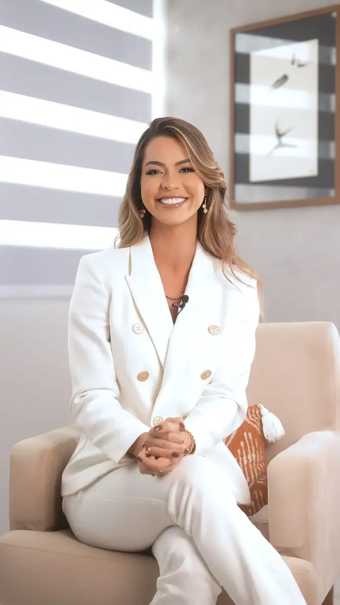 Mulher sorridente com terno branco sentada em uma poltrona bege