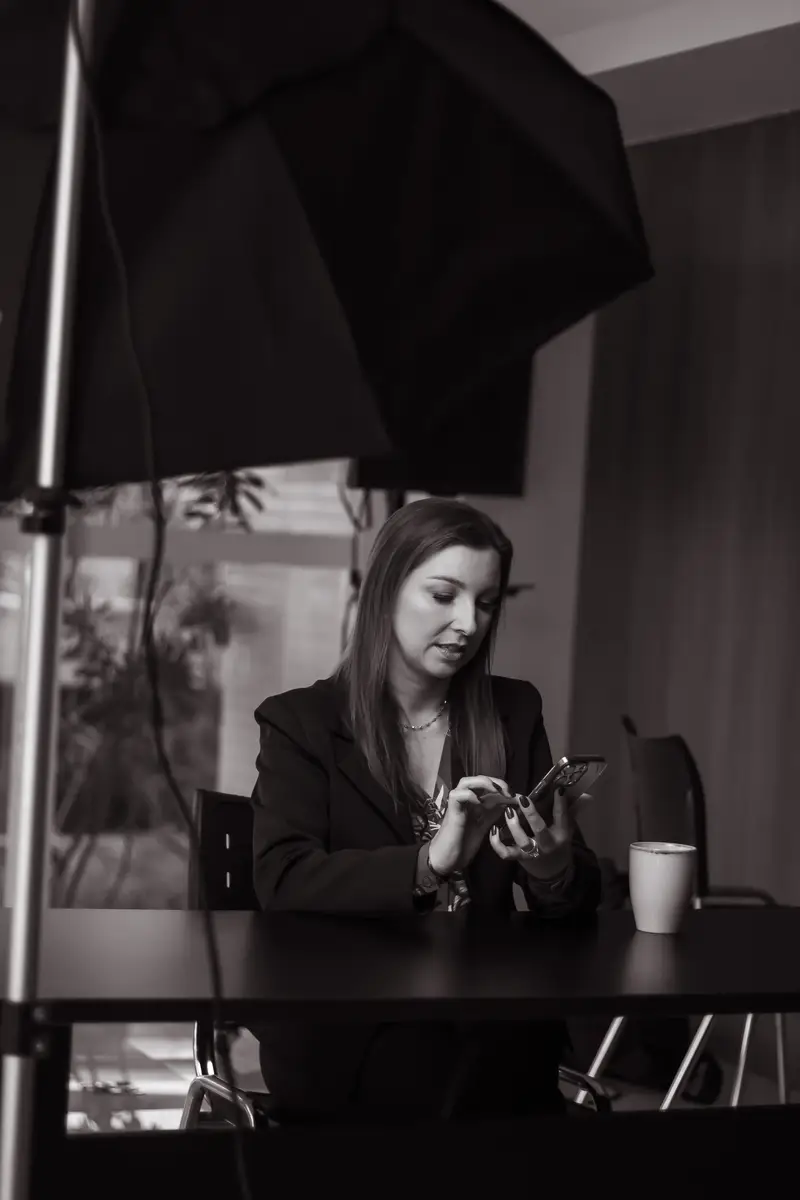 Cris Klein sentada à mesa usando smartphone com xícara ao lado