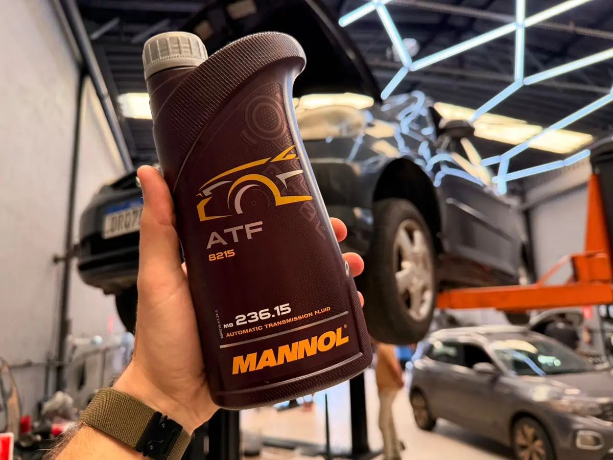Mão segurando frasco de óleo de câmbio automático Mannol ATF 8215 na oficina automotiva
