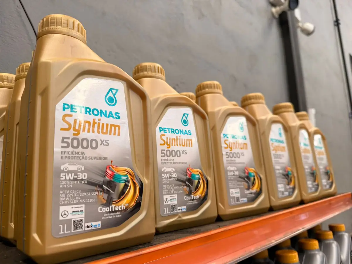 Vários frascos de óleo sintético Petronas Syntium 5000XS 5W-30 alinhados em prateleira laranja