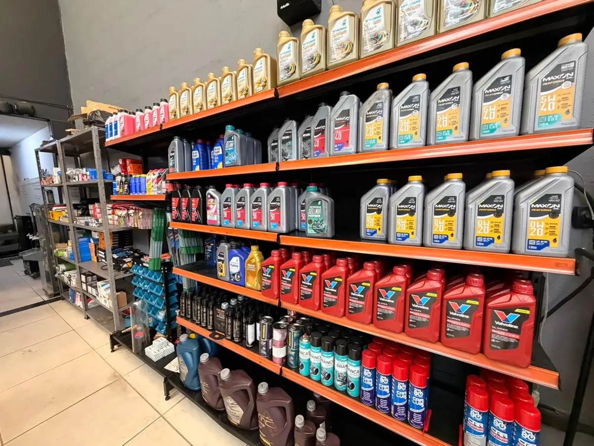 Prateleira com diversos óleos lubrificantes para automóveis organizados em fileiras dentro da oficina Megap Lub Auto Center.