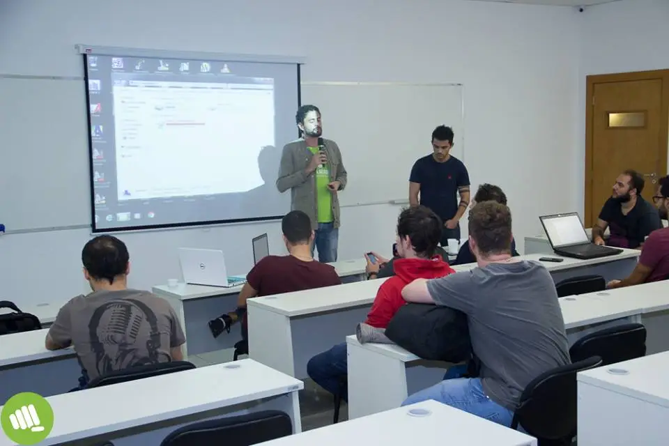 Palestrante apresentando conteúdo a uma audiência em sala de aula com projetor ligado