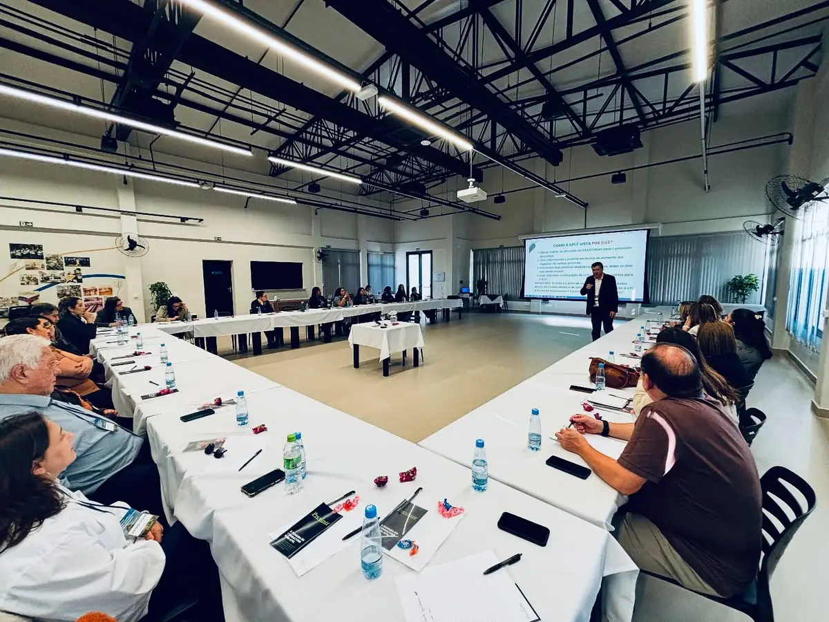 Pessoas sentadas em formato de U participando de palestra em sala ampla e iluminada