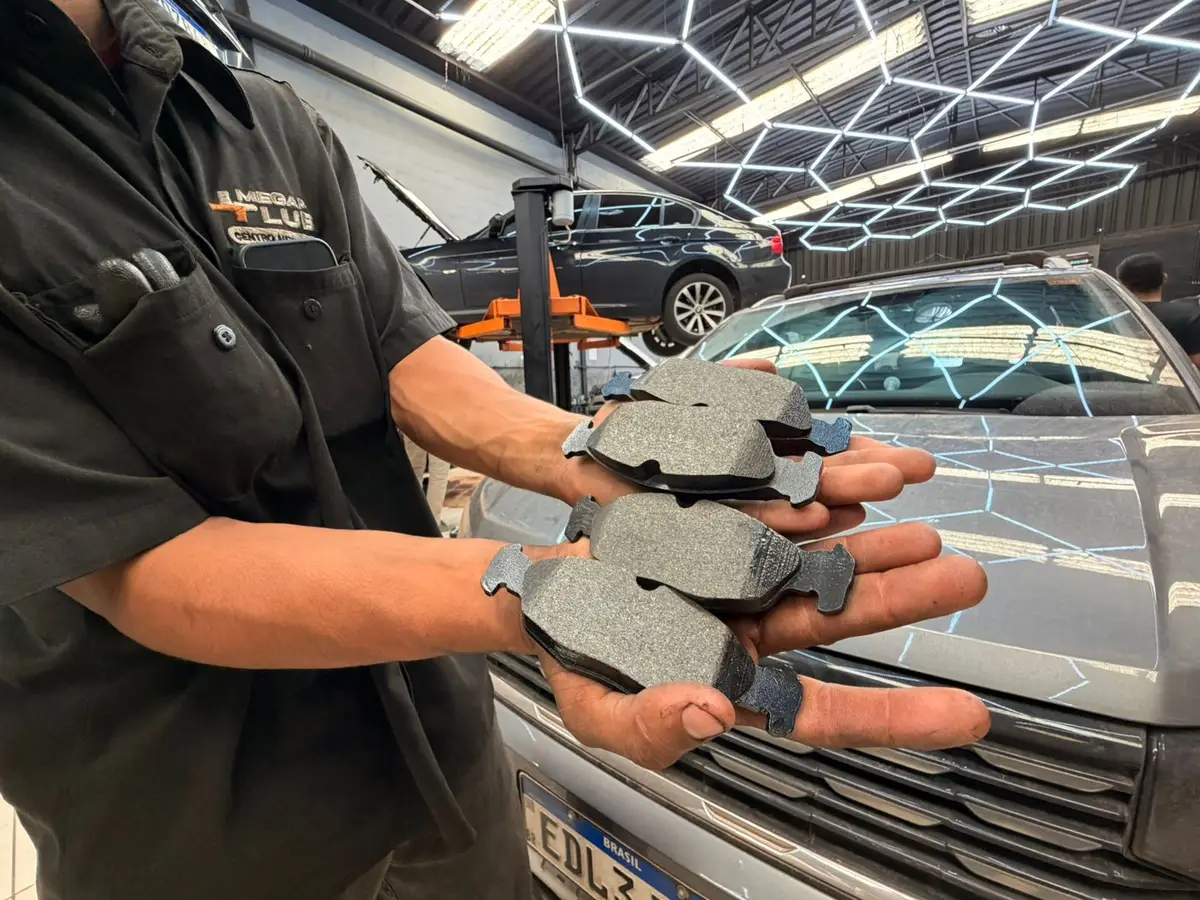 Mãos de técnico segurando pastilhas de freio novas dentro da oficina automotiva