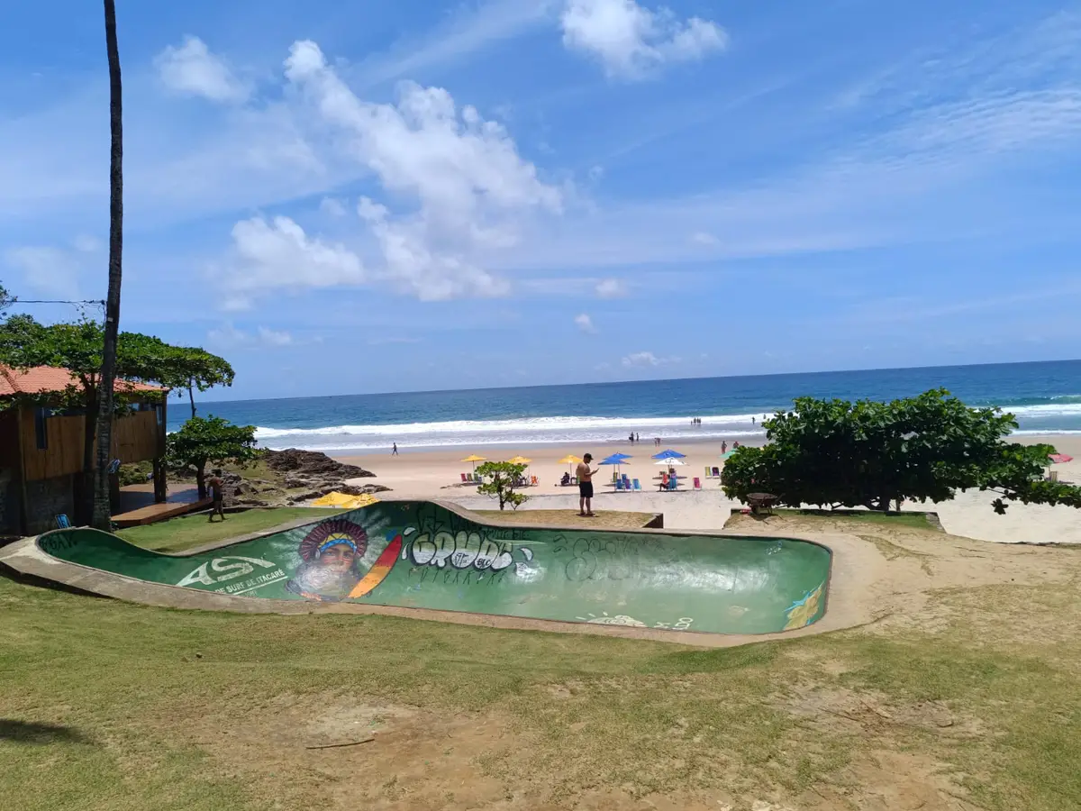 Pista de skate verde com grafite próxima à praia com guarda-sóis coloridos e mar azul ao fundo