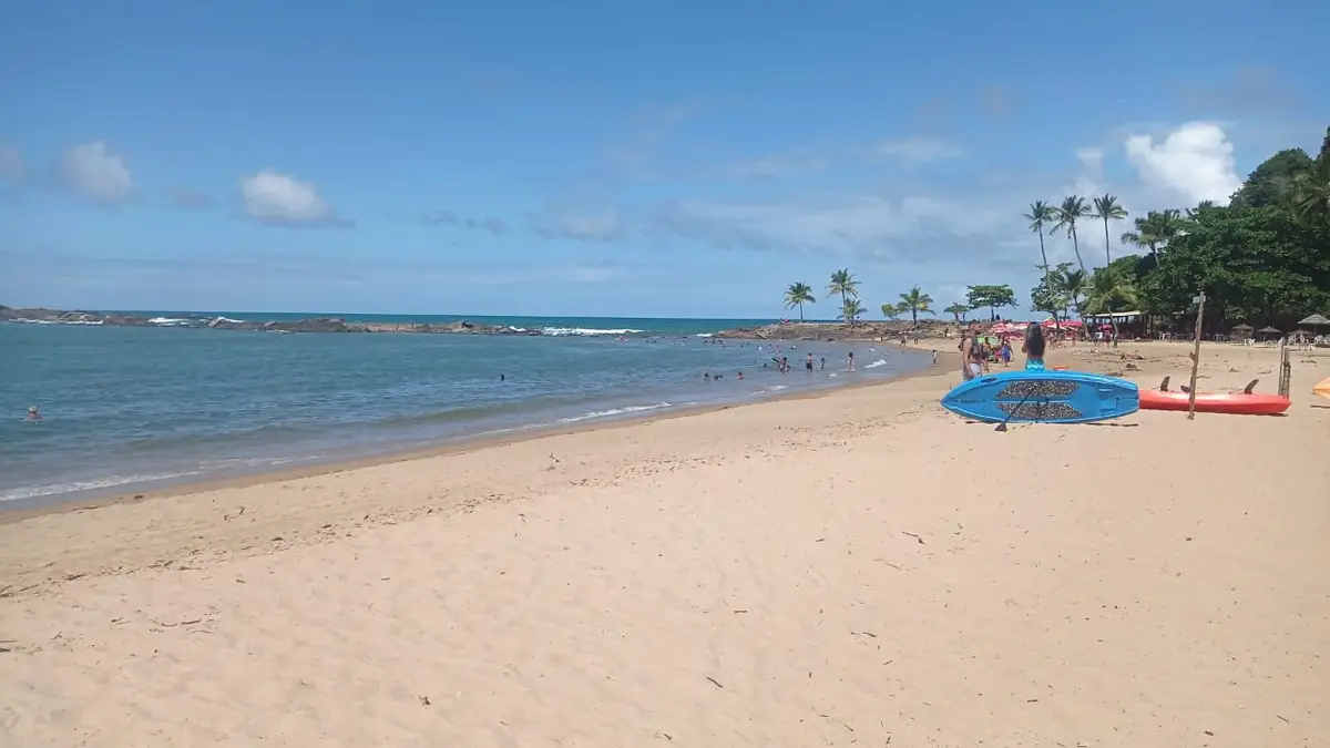 Praia com areia clara, pessoas na água e caiaques na beira da praia