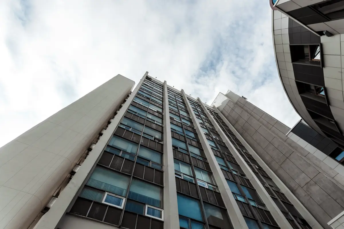 Perspectiva de prédio comercial alto visto de baixo para cima com céu nublado ao fundo