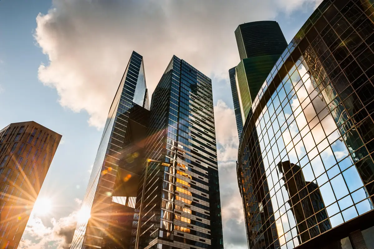 Prédios corporativos altos com fachadas de vidro refletindo o céu e o sol