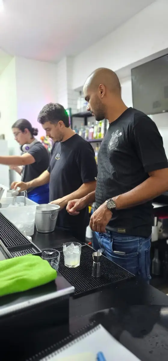 Três homens preparando drinks em um balcão de bar em ambiente de escola de bartenders