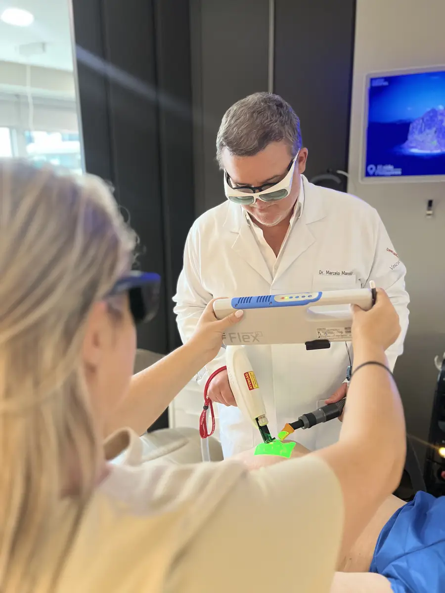 Dr. Marcelo Mandelli e assistente utilizando equipamento de laser em procedimento vascular com óculos de proteção