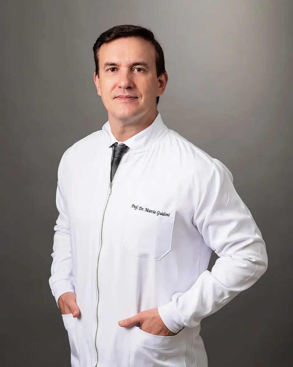 Homem de jaleco branco com mãos nos bolsos e fundo cinza