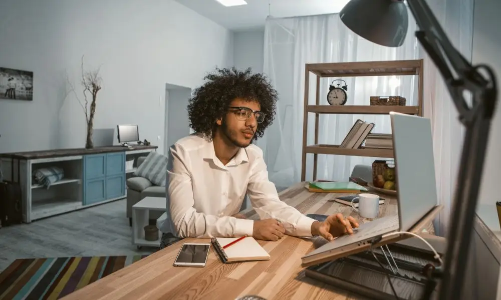 Profissional de tecnologia trabalhando em computador com caderno e celular ao lado