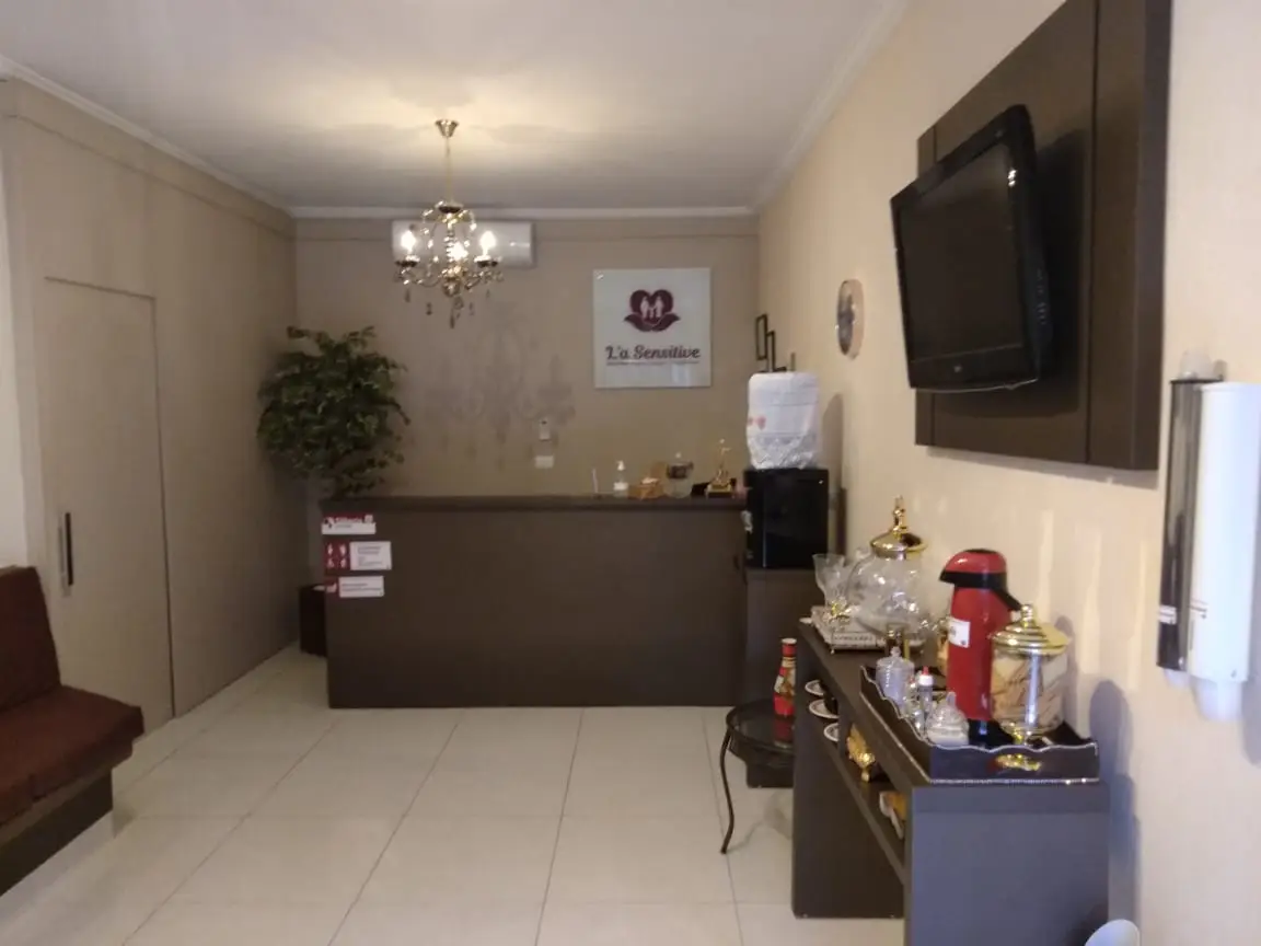 Recepção aconchegante da clínica L'a Sensitive com balcão, sofá, TV e mesa com utensílios para café e água