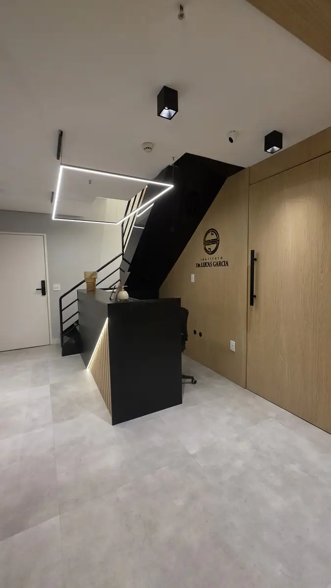 Recepção moderna do Instituto Doutor Lucas Garcia com balcão preto iluminado e parede de madeira com logo da clínica