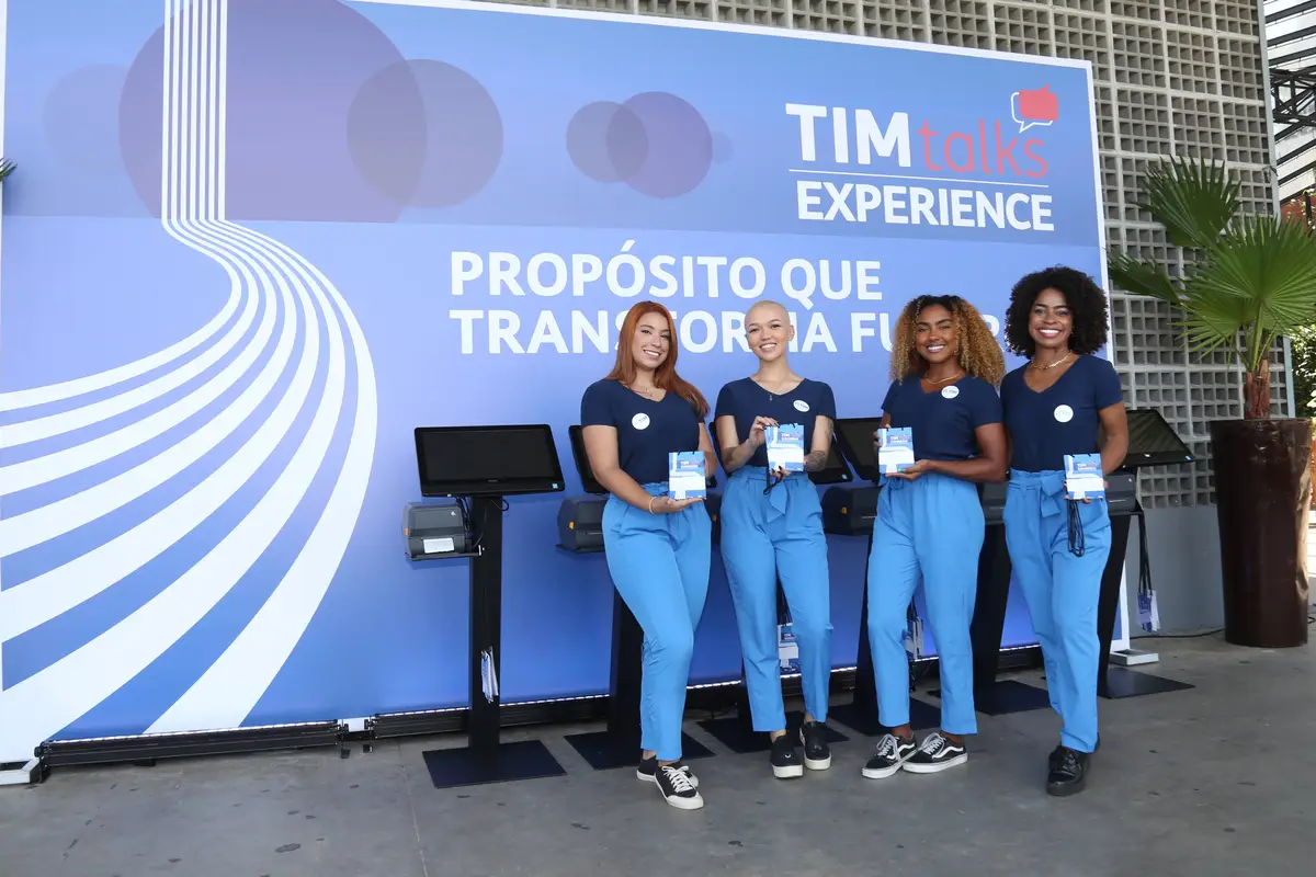 Quatro recepcionistas com uniforme azul posando em evento corporativo da TIM talks Experience