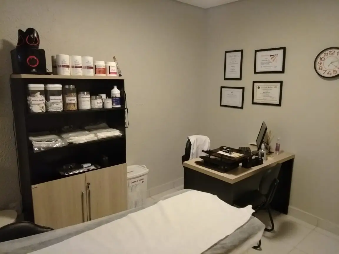 Sala de clínica médica com mesa de atendimento, prateleira com produtos e diplomas na parede