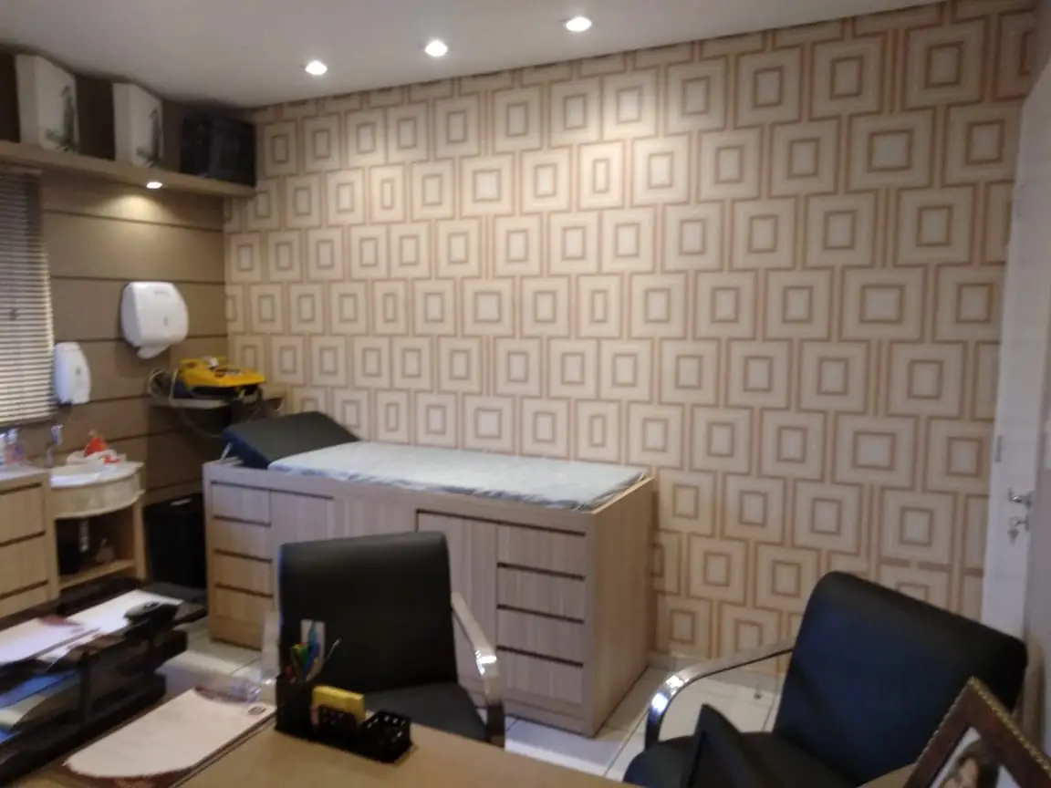 Sala de consulta médica com duas cadeiras pretas e cama de exame com gavetas de madeira clara