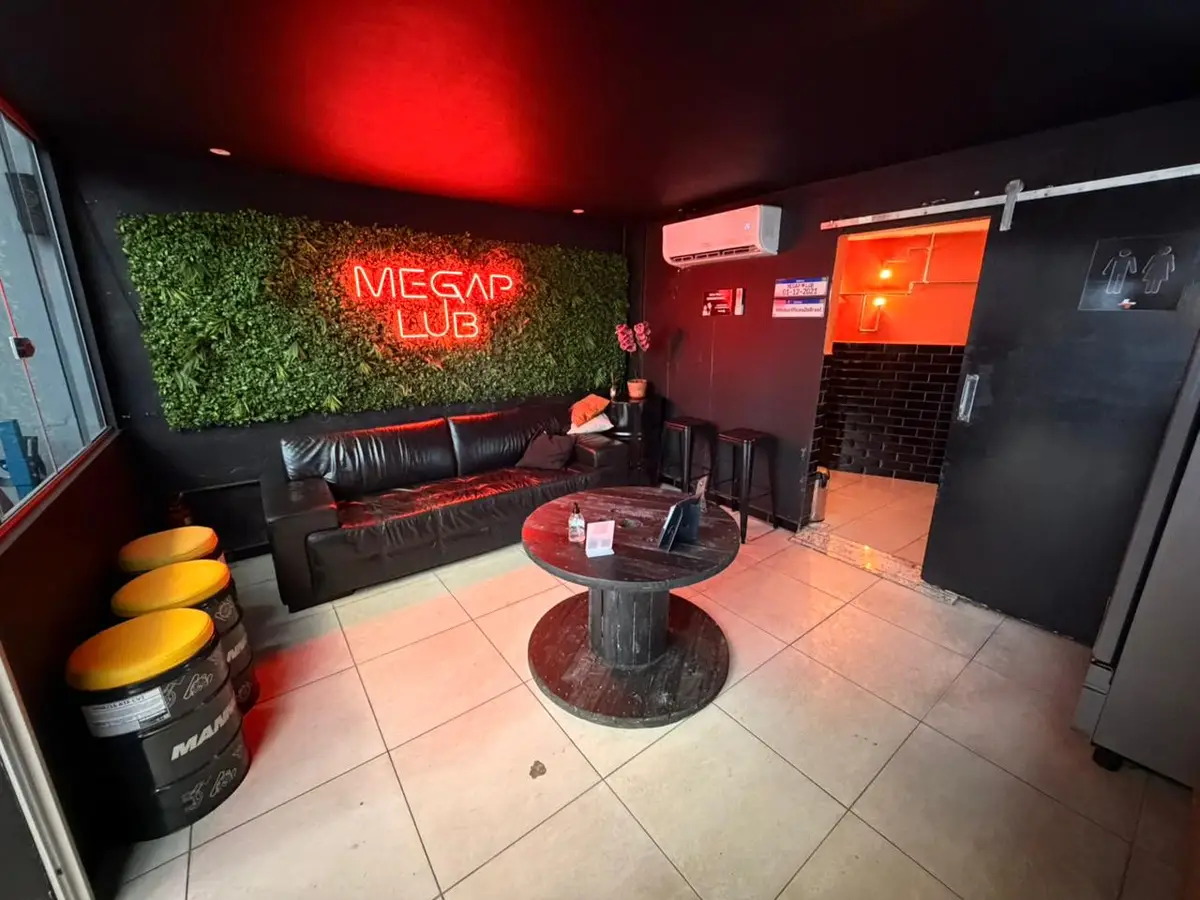 Sala de espera da Megap Lub com sofá preto, mesas de tambor e placa neon vermelha