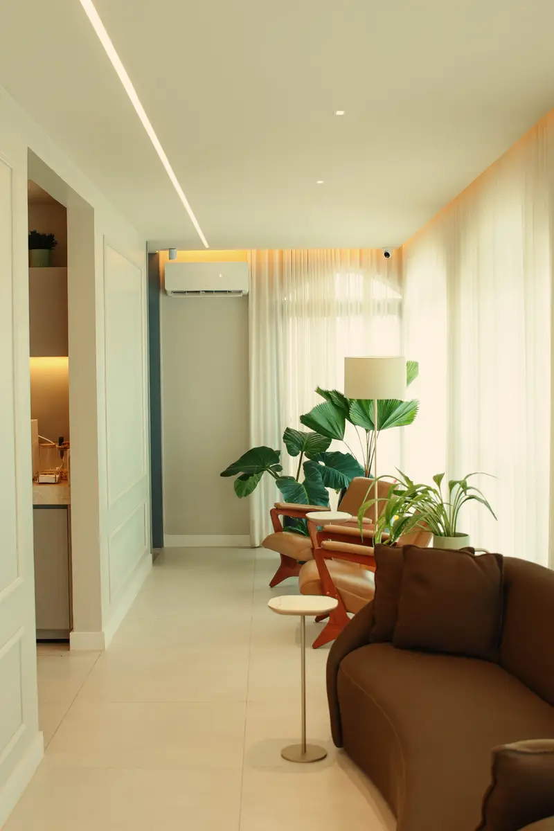 Sala de espera moderna com poltronas de couro marrom, plantas verdes e iluminação natural suave
