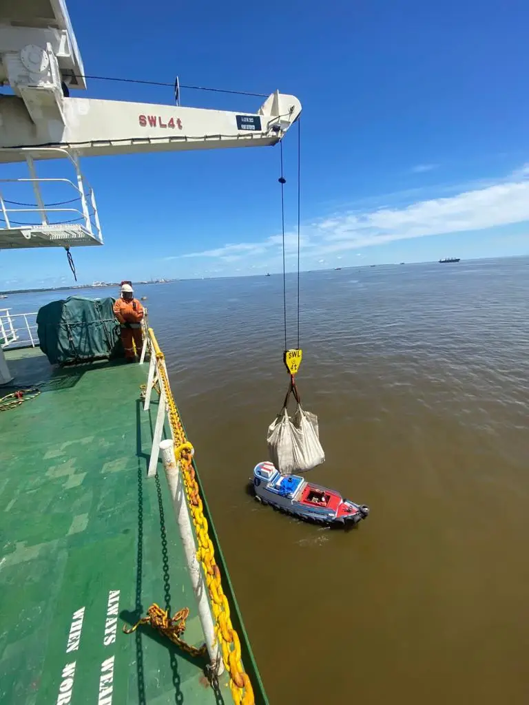 Crane lifting a heavy load over water near a ship deck with a worker in safety gear