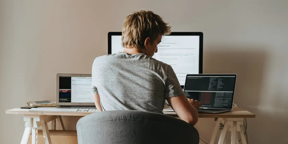Pessoa trabalhando com múltiplos computadores em uma mesa branca simples