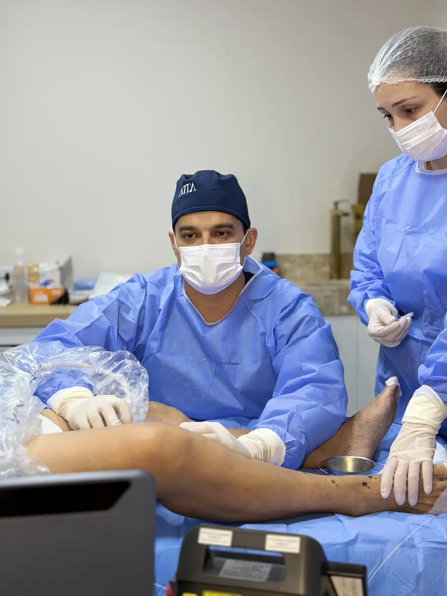 Médico vascular e assistente realizando procedimento em perna de paciente com varizes