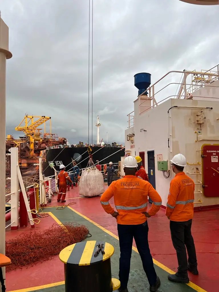 Crew wearing safety helmets and orange tropical ship supply jackets overseeing cargo handling on a ship deck