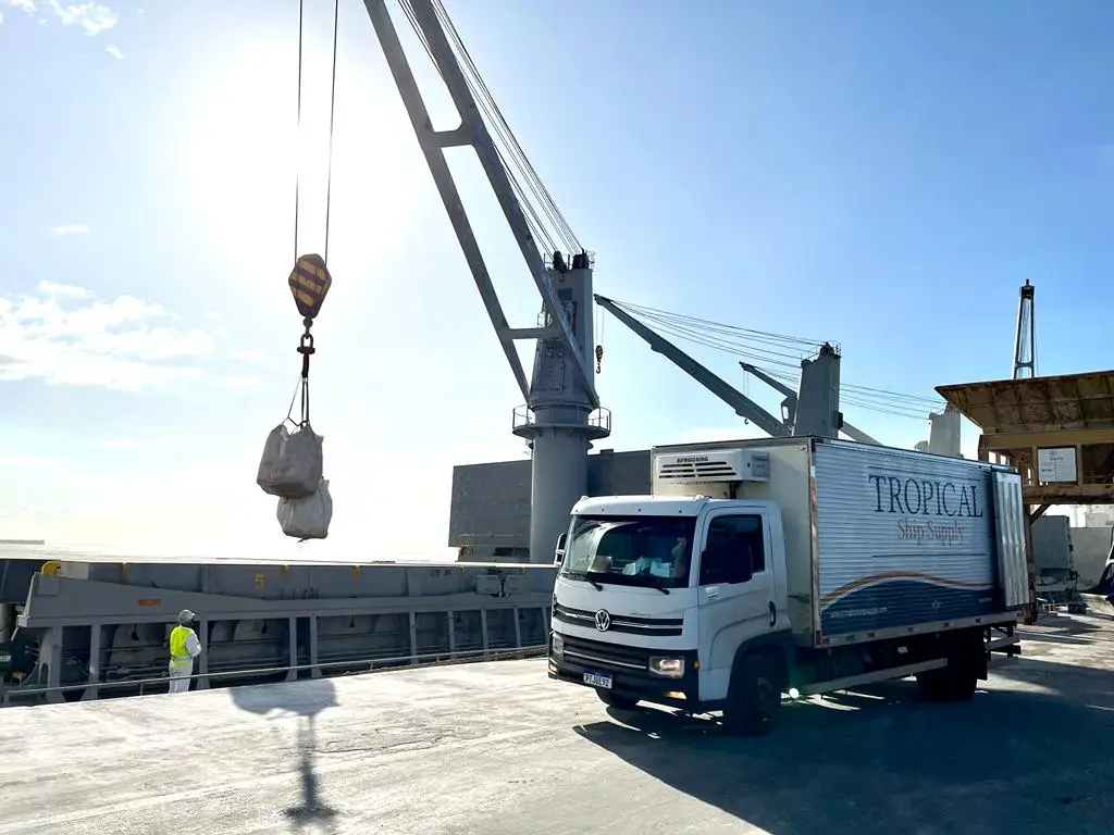 Tropical Ship Supply delivery truck unloading cargo at a port with crane lifting goods